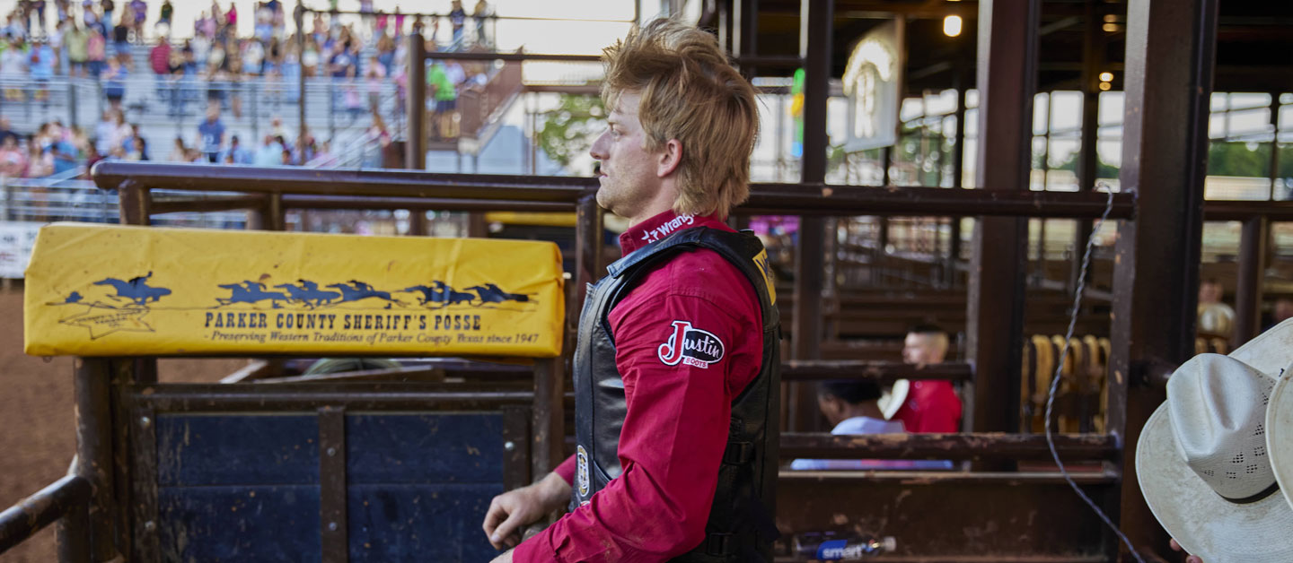 Cowboy wearing a red shirt standing on the bucking chutes at a rodeo.